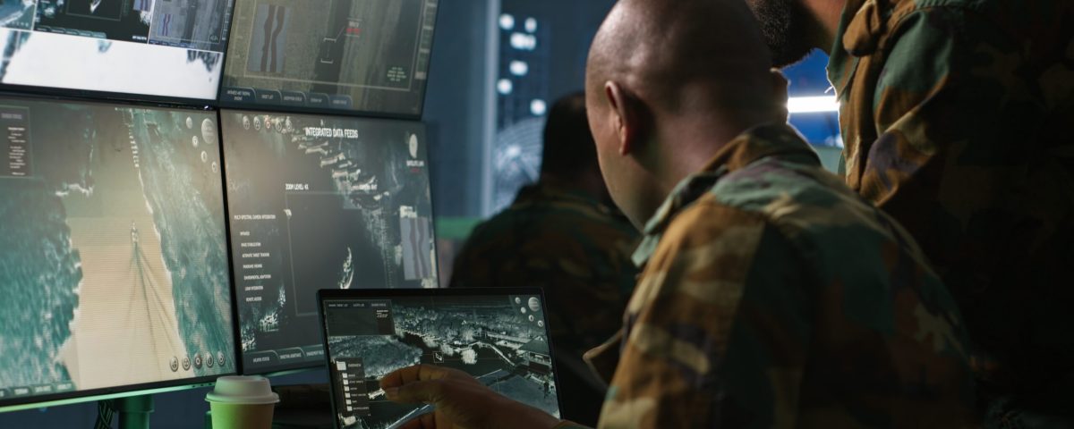 Military soldier in mission control center, overseeing national safety operations using notebook next to colleague. Team of army specialists examining data in monitoring room command center, camera A